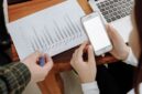 Seorang pengusaha sedang menganalisis data digital di layar tabletnya, menunjukkan fokus pada strategi berbasis data untuk mengoptimalkan kinerja bisnis. Latar belakang kota modern merepresentasikan lingkungan bisnis yang dinamis dan terhubung.