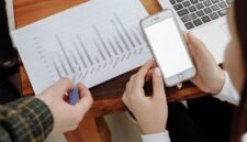Seorang pengusaha sedang menganalisis data digital di layar tabletnya, menunjukkan fokus pada strategi berbasis data untuk mengoptimalkan kinerja bisnis. Latar belakang kota modern merepresentasikan lingkungan bisnis yang dinamis dan terhubung.