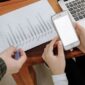 Seorang pengusaha sedang menganalisis data digital di layar tabletnya, menunjukkan fokus pada strategi berbasis data untuk mengoptimalkan kinerja bisnis. Latar belakang kota modern merepresentasikan lingkungan bisnis yang dinamis dan terhubung.