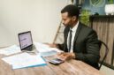 Seorang pengusaha muda tampak fokus menganalisis laporan keuangan di meja kerjanya, menunjukkan pentingnya perencanaan matang dalam mengelola modal usaha. Meja dipenuhi peralatan kantor dan laptop, mencerminkan aktivitas bisnis modern yang efisien.