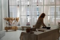 Seorang perempuan sedang sibuk merangkai bunga di meja kerjanya yang tertata rapi di sudut rumah, menggambarkan bagaimana hobi dapat diubah menjadi usaha rumahan yang produktif. Ruangan tersebut dipenuhi dengan berbagai jenis bunga segar dan alat-alat merangkai, menunjukkan suasana kreatif yang mendukung pengembangan bisnis.
