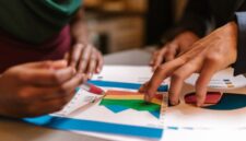 Sebuah tim sedang berdiskusi intens di depan layar monitor yang menampilkan berbagai grafik dan data analitik, menggambarkan proses perencanaan strategi bisnis digital yang komprehensif. Momen ini merefleksikan pentingnya kolaborasi dan data dalam mengambil keputusan strategis di era digital.