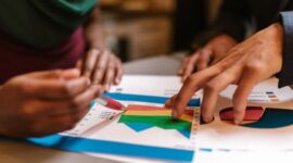 Sebuah tim sedang berdiskusi intens di depan layar monitor yang menampilkan berbagai grafik dan data analitik, menggambarkan proses perencanaan strategi bisnis digital yang komprehensif. Momen ini merefleksikan pentingnya kolaborasi dan data dalam mengambil keputusan strategis di era digital.