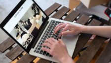 Seorang pemilik UMKM sedang mengoperasikan laptopnya di sebuah kedai kopi yang nyaman, menggambarkan dedikasi dalam mengelola pemasaran online produk lokalnya. Gambar ini merefleksikan bagaimana teknologi menjadi alat vital bagi pelaku usaha kecil untuk mengembangkan jangkauan pasar mereka.